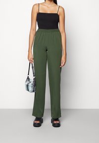 Groene, lichtgewicht broek met wijde pijpen en een elastische tailleband. Gecombineerd met een zwart spaghettihemdje en zwarte grove plateauzandalen.