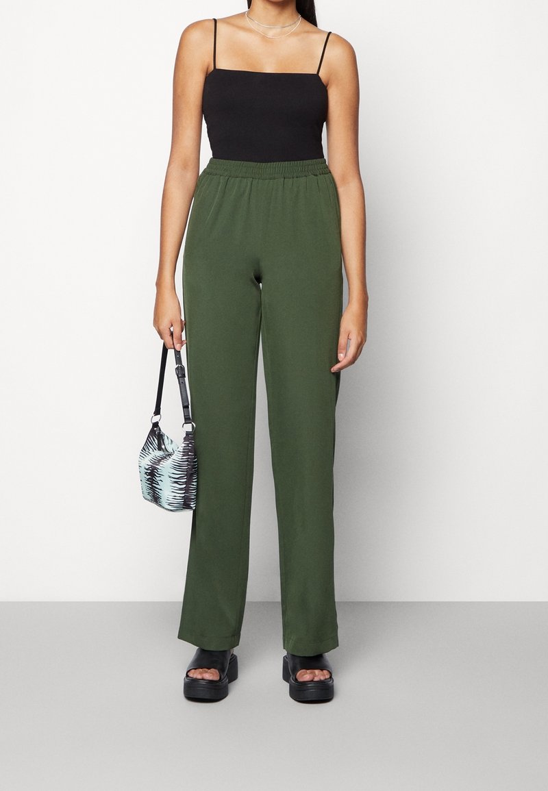 Groene, lichtgewicht broek met wijde pijpen en een elastische tailleband. Gecombineerd met een zwart spaghettihemdje en zwarte grove plateauzandalen.