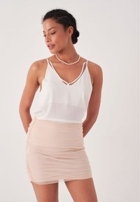 Top bianco senza maniche con scollatura a V profonda e spalline sottili, abbinato a una mini gonna aderente e arricciata di un delicato rosa chiaro.
