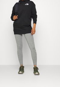 Svart huoodie, grå leggings och gröna träningsskor. Hoodien har en logotyp; leggingsen är figurnära med ett fläckigt mönster.