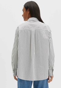 Weißes und navyblau gestreiftes Hemd mit Kragen, Knopfmanschetten und Rückenfalte. Hergestellt aus leichtem Stoff, mit geradem Schnitt und legerer Passform.