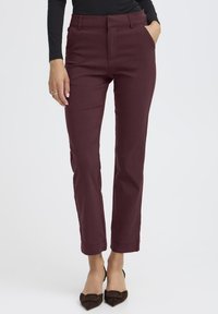 Bordeauxkleurige broek met een tailored fit, voorzakken en een soepele textuur. Afgewerkt met een omgeslagen zoom boven de enkel, gecombineerd met donkere hakken.