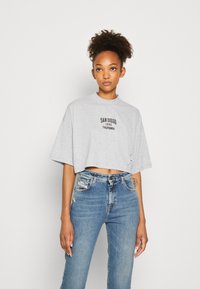 Gray cropped t-shirt with a round neck and a printed graphic, paired with blue high-waisted jeans featuring a distressed texture and patches.