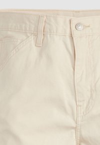 Pantaloni in cotone beige con taglio dritto, chiusura con zip e bottone, passanti per cintura e dettagli di cucitura discreti vicino alle tasche.
