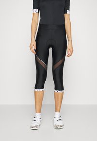 Leggings de ciclismo pretos com um design ajustado, apresentando painéis de malha e detalhes em bolinhas brancas na bainha. Textura suave, corte até o joelho.