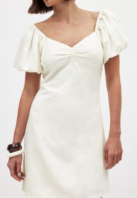 Weißes Leinenkleid mit Puffärmeln, tiefem V-Ausschnitt und gerafftem Detail vorne. Glatte Textur mit lockerer Passform und seitlichen Schlitzen.