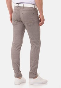 Gestreifte, graue Hose mit schlanker Passform, ausgestattet mit einem weißen Gürtel und Gesäßtaschen mit einem dezenten Detail. Getragen mit weißen Sneakers.