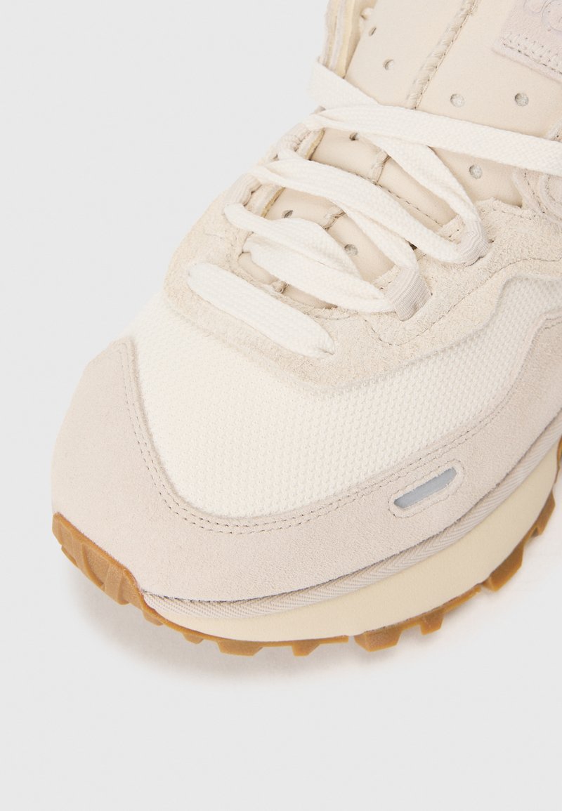 Beige Sneaker mit einem strukturierten Mesh-Obermaterial, Wildlederakzenten und einer Gummisohle mit Traktionsmustern. Schnürdesign mit sichtbaren Nähten.