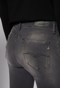 Vaqueros elásticos grises con un diseño ajustado, que cuentan con dos bolsillos traseros y detalles de costura sutiles. La etiqueta en la cinturilla dice "REPLAY HYPERFLEX".