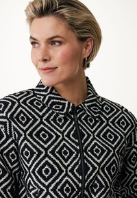 Zip-up jacka i svart och vitt, med ett geometriskt diamandmönster, krage, vävd textur och synlig dragkedjedetalj.
