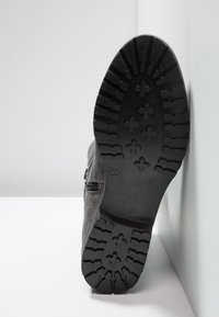 Bottine en suède noire avec une semelle en caoutchouc texturée affichant des profils profonds. Détail de fermeture éclair sur le côté, taille marquée comme 37.