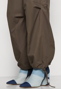 Brązowe tapered spodnie z elastycznymi mankietami, w połączeniu z niebieskimi i jasnoniebieskimi szpilkami w kolorze blokowym z ostrym noskiem i teksturowaną tkaniną.