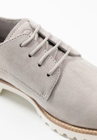 Scarpa in suede grigia con cinque occhielli per i lacci, suola in gomma bianca e finitura testurizzata. Presenta cuciture a contrasto lungo il bordo.