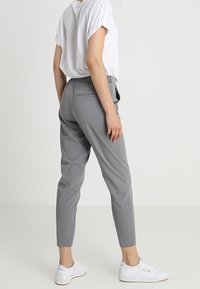 Grijze op maat gemaakte broek met een slim fit, elastische tailleband en zijzakken, gecombineerd met een witte T-shirt met korte mouwen en witte sneakers.