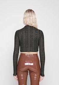 Černý zkrácený svetr s ribrovou texturou a dlouhými rukávy, spárovaný s lesklými hnědými kalhotami s vysokým pasem. Přední pohled ukazuje celé oblečení.