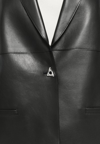 Mustmust nahkblazer, millel on nurgatagune krae, koos kolmnurkse hõbedase metallaktsendiga ja esikätega. Sile tekstuur ja kohandatud disain.