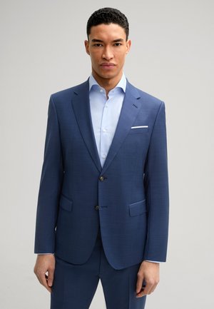 Marineblaues Blazer mit strukturierter Oberfläche, einreihigem Design, mit Reverskragen und zwei Fronttaschen. Kombiniert mit einem hellblauen Hemd.