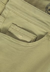 Pantaloni din bumbac verde deschis, cu un buzunar frontal, având cusături tonale și un mic logo brodat pe buzunar.