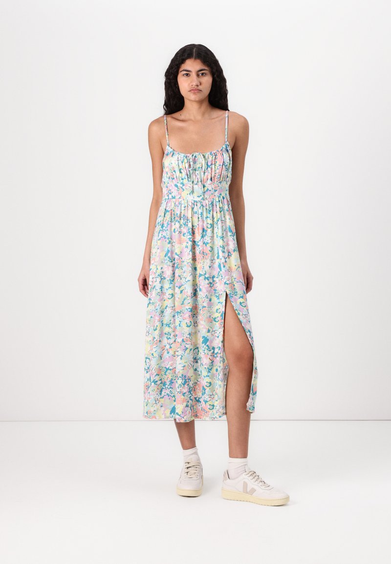 Floral maxi dress with thin straps, pastel colors, and a side slit. Made of lightweight fabric, featuring a gathered bodice and flowing design.
