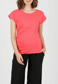 Korallenfarbiges T-Shirt mit kurzen Ärmeln, aus weicher Baumwolle, mit einem runden Halsausschnitt und lockerer Passform, kombiniert mit schwarzen, weit geschnittenen Hosen.