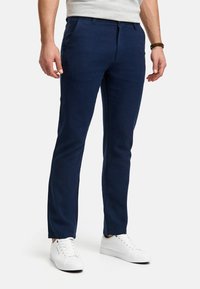 Pantaloni slim-fit de culoare bleumarin, confecționați dintr-un material ușor, având buzunare laterale și o textură netedă, asortați cu adidași albi.