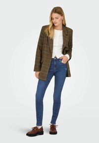 Pruun ruuduline bleiser valge särgi peal, kombineeritud siniste kitsaste teksade ja pruuni lõhikuga kingadega mustade talladega. Sile tekstuur, struktureeritud istuvus.