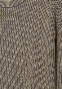 Gros plan d'un tissu tricoté serré avec motif côtelé vertical en beige et gris atténués.