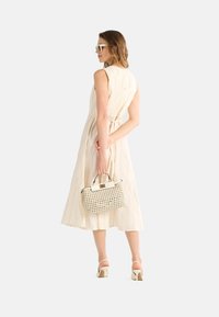 Abito senza maniche di un beige chiaro, con righe verticali, vita segnato e gonna fluida. Abbinato a una borsa intrecciata e sandali con tacco a blocco bianchi.