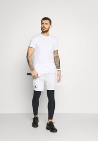 White t-shirt, white shorts with black logo, black leggings, and black athletic shoes. Holding a white tennis racket. Simple design.