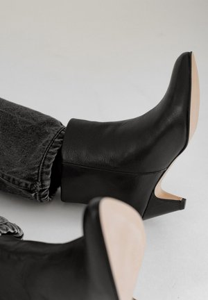 Schwarze Lederstiefeletten mit einem schmalen hohen Absatz, die eine glatte Textur und ein minimalistisches Design aufweisen, kombiniert mit dunkler Jeans.