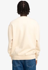 Lichtbeige sweatshirt met een zachte textuur, ronde hals, ribbels aan de mouwen en een relaxte pasvorm, gecombineerd met blauwe denim jeans.