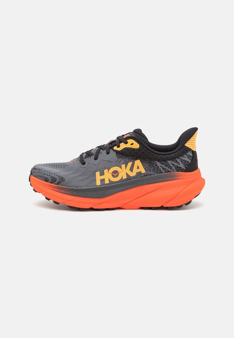 Šedá běžecká bota s oranžovou mezipodešví a černými akcenty. Má strukturovaný svršek, výrazné logo a odolnou gumovou podešev.