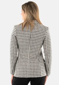 Blazer in fantasia houndstooth bianco e nero, con vestibilità tailored, spalle strutturate e tessuto testurizzato, con orlo leggermente sfrangiato.