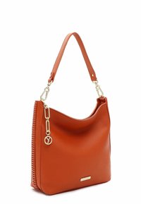 Borsa in pelle arancione con forma curvata, superficie texturizzata e dettagli in oro. Presenta un lato intrecciato e un ciondolo decorativo con logo.