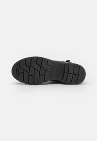 Semelle de chaussure en caoutchouc noir avec un motif de texture, présentant de profonds sillons pour l'adhérence et une section de talon lisse et plate.