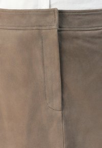 Detailní záběr na dvě semišové sukně v béžových a taupe odstínech, zobrazující přední pas a detaily bočního švu.