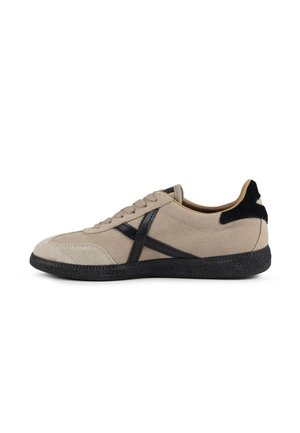 Zapatilla de ante beige con suela negra y diseño negro en forma de X en el lateral, cierre de cordones y detalle negro en el talón.