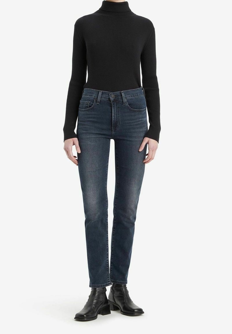 Svart ribbad polotröja kombinerad med mörkblå jeans med hög midja och svarta ankellåga stövlar. Enkel design med figurnära silhuett.