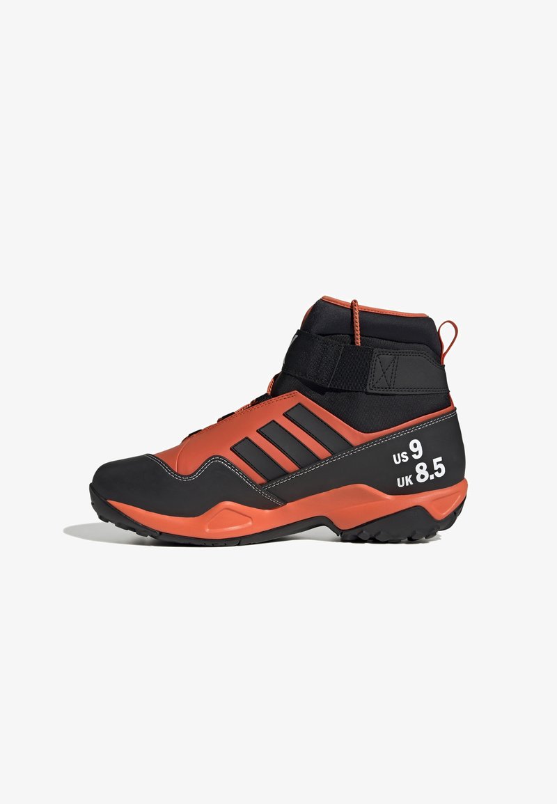 Chaussure de sport montante noir et orange avec semelle extérieure en caoutchouc, trois bandes noires et marquages de taille en blanc sur le talon. Finition texturée.