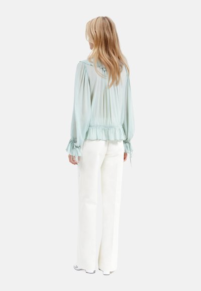 Blusa azzurro chiaro con maniche ampie e orlo arricciato, abbinata a pantaloni bianchi a gamba larga. Tessuto morbido e fluido con una vestibilità rilassata.