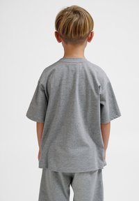 Graues Baumwoll-T-Shirt mit kurzen Ärmeln, lockerer Passform und Rundhalsausschnitt, getragen mit passenden grauen Hosen, von hinten betrachtet.