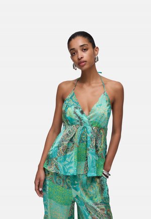 Donna che indossa un top halter paisley turchese e pantaloni a gamba larga coordinati, accessoriata con orecchini a cerchio in argento e braccialetti.