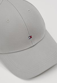 Gorra de béisbol de algodón gris claro con detalles de costura y un pequeño logotipo bordado que presenta acentos en rojo, blanco y azul.