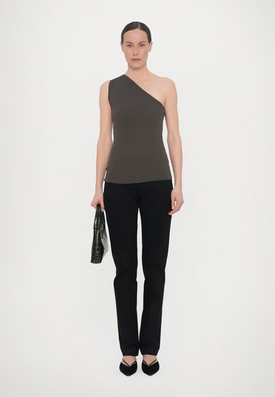 Top canelado de um ombro em castanho-escuro, combinado com calças skinny pretas e sapatos de salto agudo pretos. A modelo segura uma mala texturizada verde.