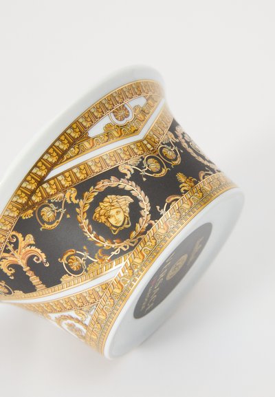 Kerámia tál fekete háttérrel, finom arany és fehér barokk mintákkal, kör alakú motívumokkal és egy arccal a közepén.