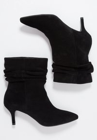 Bottes cheville en daim noir avec un bout pointu, une tige douce et froncée, et un talon fin. Texture lisse sans éléments métalliques visibles ni motifs.