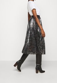 Falda negra con lentejuelas, con pliegues y un acabado metálico, combinada con una camiseta blanca y botas negras de tacón alto hasta la rodilla.