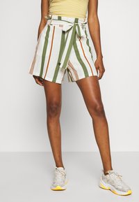 Shorts rayés en blanc, vert et orange avec une taille haute et un détail de ceinture nouée. Fabriqués en tissu léger pour plus de confort.