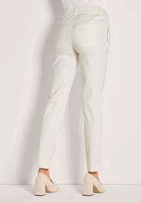 Witte, op maat gemaakte broeken met een gladde textuur, voorzien van achterzakken en een met rits afgesloten accentzak. Gecombineerd met lichtbeige block-heeled schoenen.