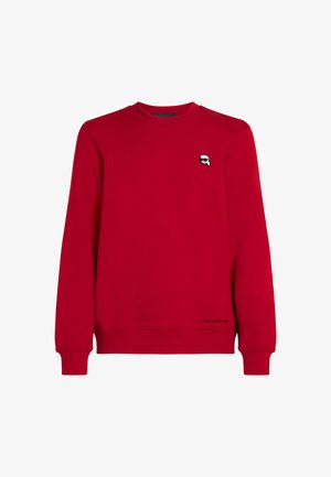 Rdeča majica s kapuco iz mehkega materiala, z okroglo izrezom, rebrastimi manšetami in majhnim logotipom na prsih. Klasičen dizajn, sproščen kroj.